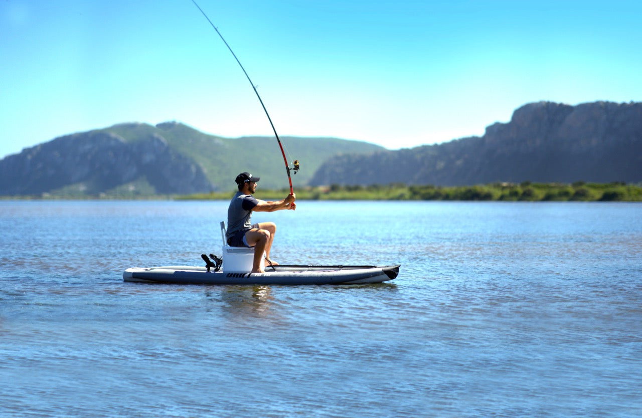 Fisherman casting a fishing rode line on inflatable paddleboard isup Drift by Aqua Marina with fishing pole. Rent fishing gear from MTBoarders.com with delivery included. Or buy now from e-boarders.com