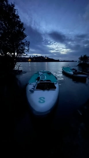 Paddleboard on a calm lake at night with a dark sky and trees in the background.