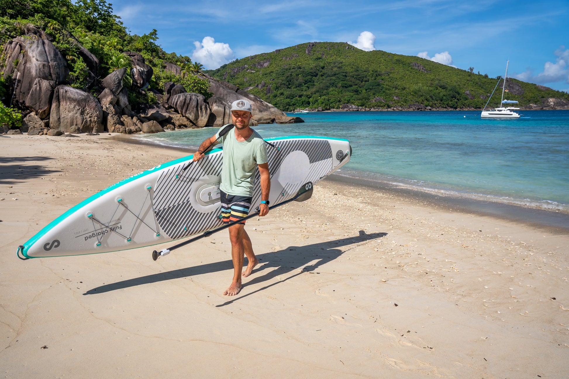 Man walks on beach carrying SipaBoards self-inflating electric paddleboard rental delivered to Flathead Valley lakefronts.