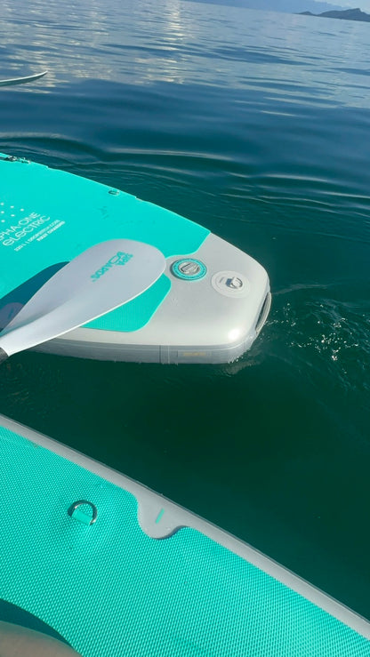 Teal inflatable electric SIPA paddle board partially submerged in water with a clear sky background