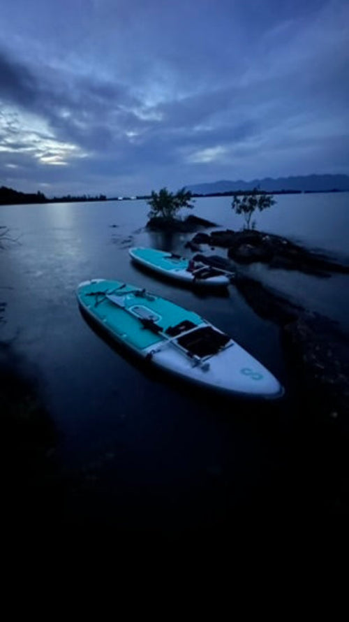 Two paddleboards on a calm lake with a dark sky and mountains in the background.