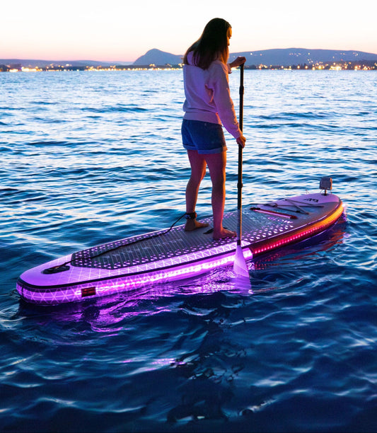 Nighttime paddler on the water riding an Inflatable LED Glow Paddleboard iSUP by Aqua Marina. Illuminates for nighttime moonlight paddle parties on the water. Rent with delivery to docks, cabins, and vacation homes in the Flathead Valley, Montana. Book with MontanaBoarders.com.